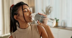 Hydration and Aging: How Proper Hydration Boosts Longevity and Brain Health, A beautiful women with dark hair drinking water out a bottle with a satisfied expression
