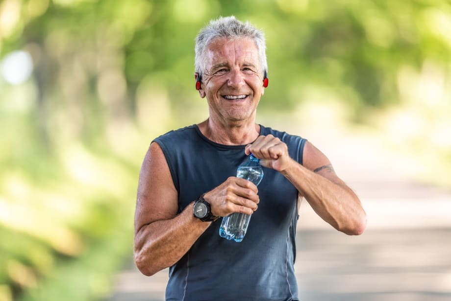  Hydration boosts longevity. An elderly person smiling while on a run and drinking water