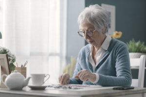 Your Brain, Your Future: Cognitive Health and Longevity, Happy senior woman playing puzzle at home alone and having tea