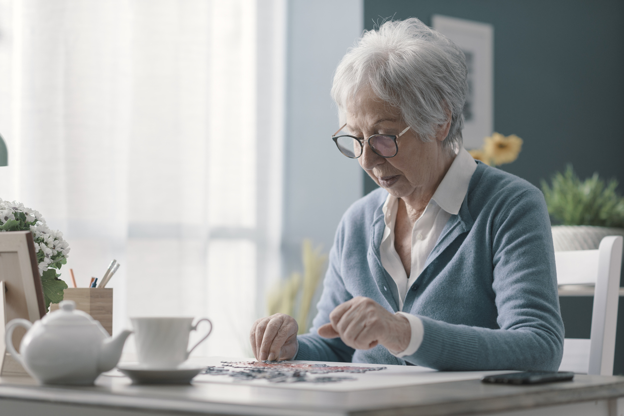 Your Brain, Your Future: Cognitive Health and Longevity, Happy senior woman playing puzzle at home alone and having tea