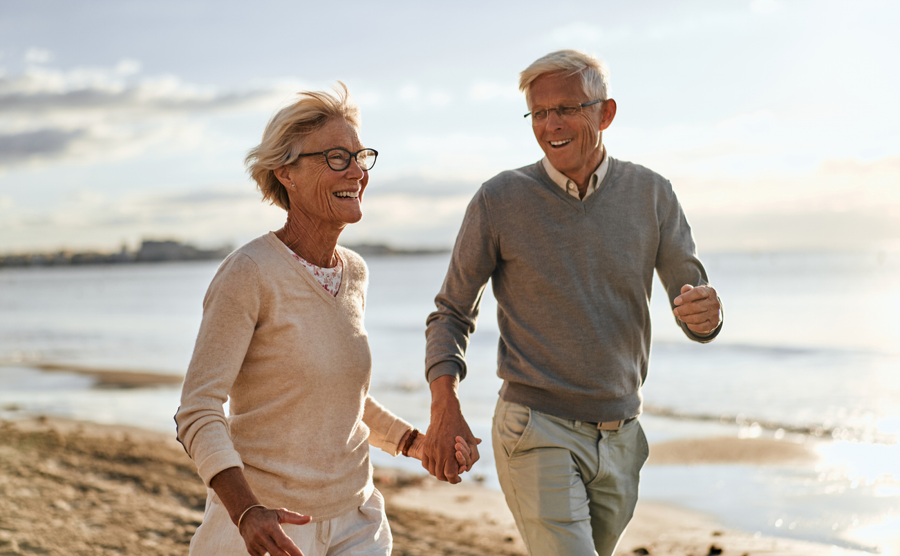 OmniWave™ Therapy in Tampa Bay: Restoring Mobility and Supporting Longevity, An older couple walking on the beach holding hands and smiling