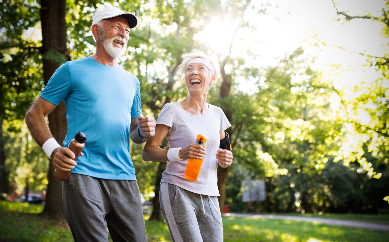 Happy senior couple jogging together in a sunny park.