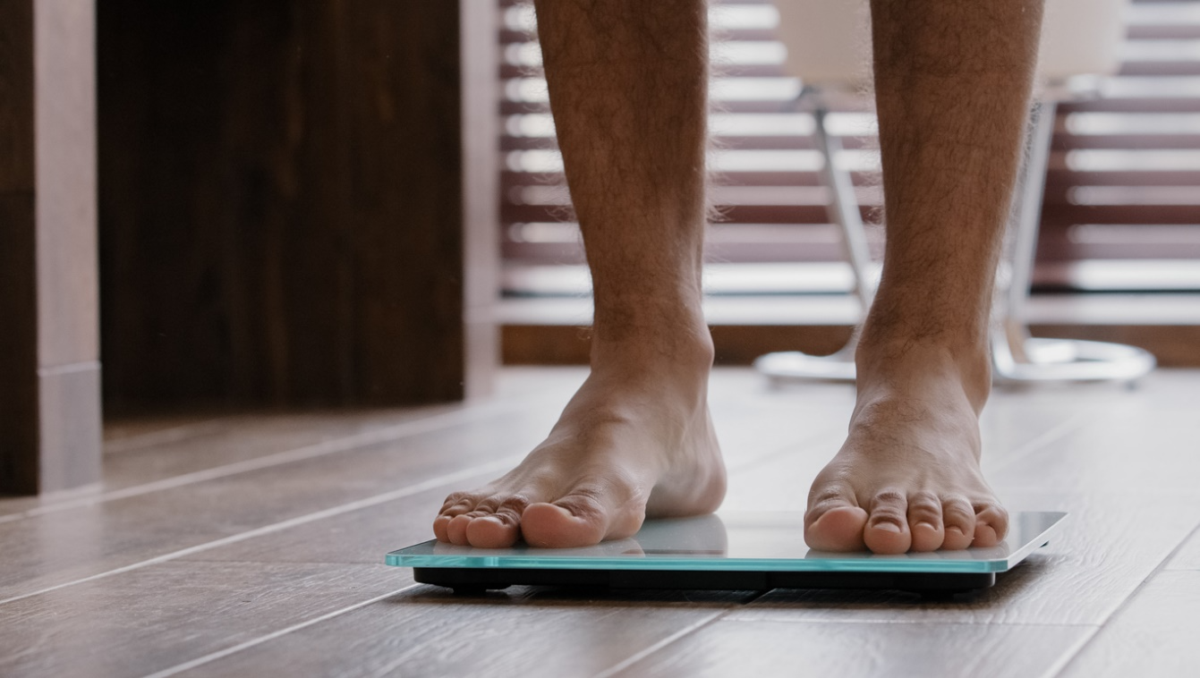 Close-up of bare feet stepping onto a digital weight scale on a tiled floor.