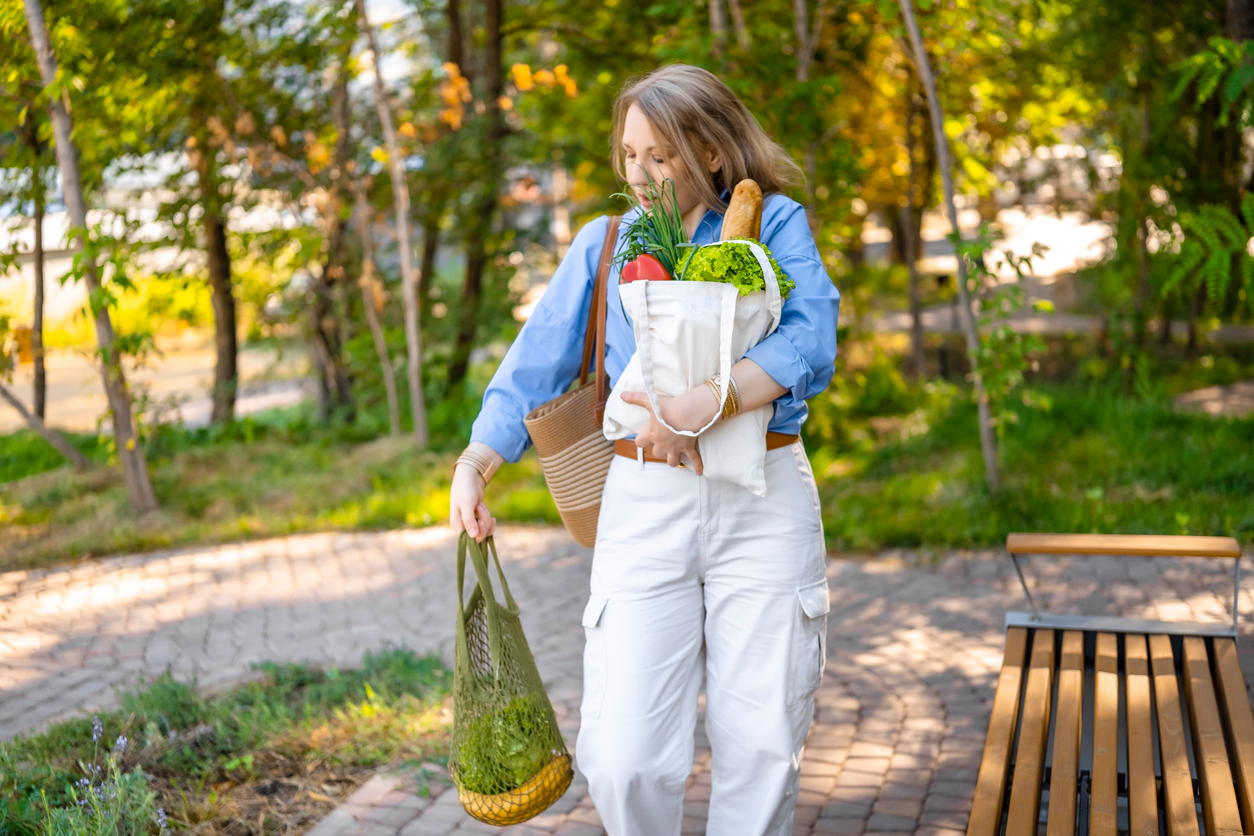 Woman carrying reusable grocery bags outdoors, illustrating the everyday strength and independence that support healthy aging.