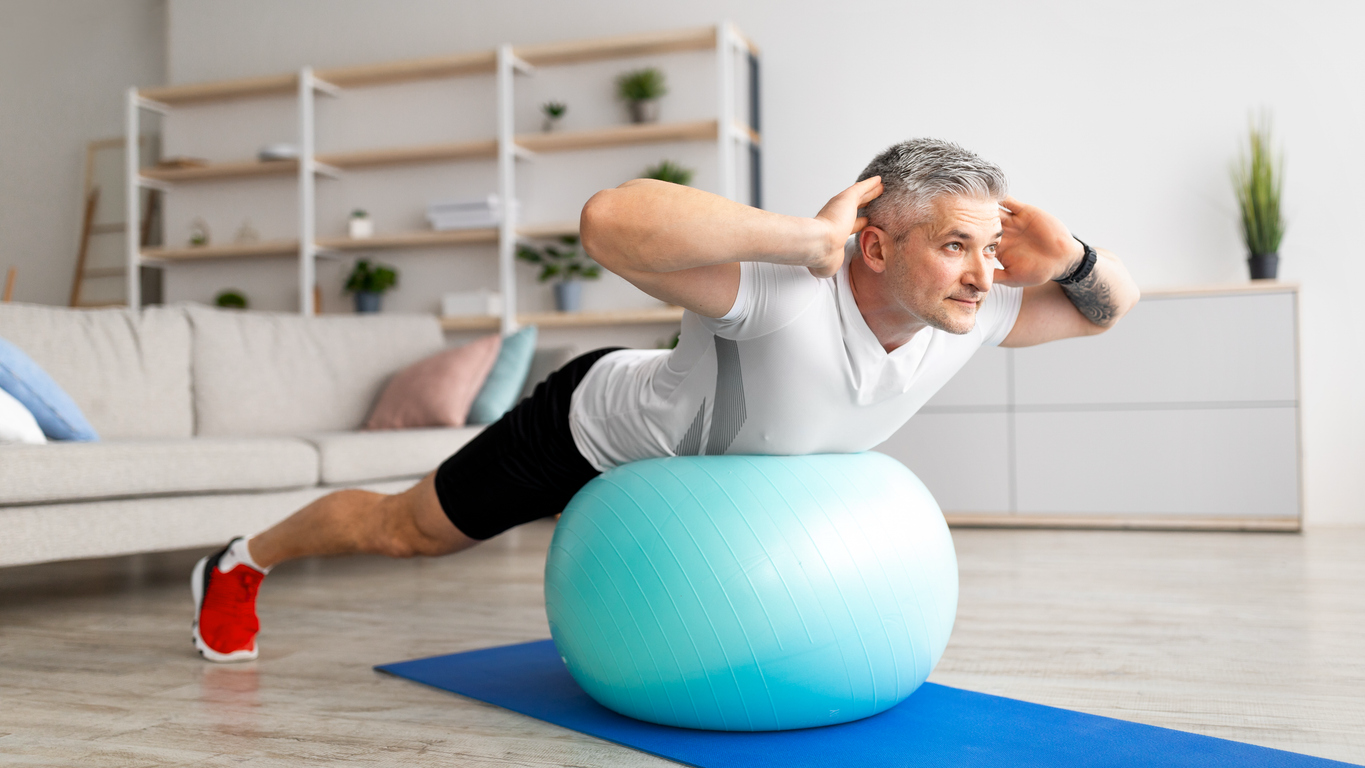 Older man performing a back extension exercise on a stability ball at home, demonstrating strength training to support healthy aging, mobility, and independence.